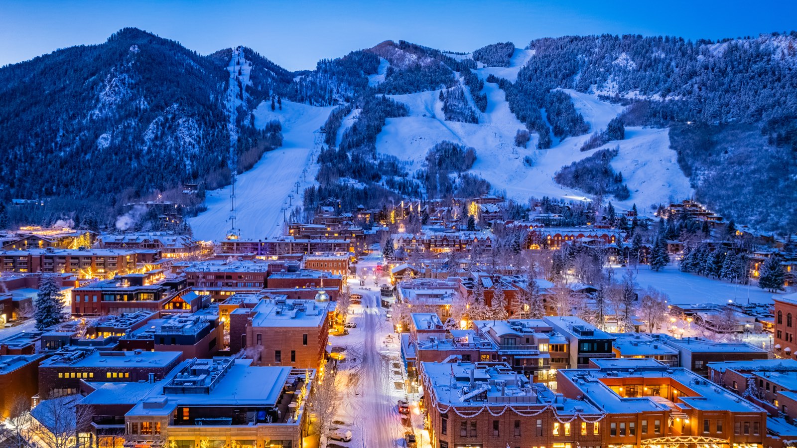Vista del pueblo de Aspen al anochecer con sus calles iluminadas y las pistas de Aspen Mountain al fondo