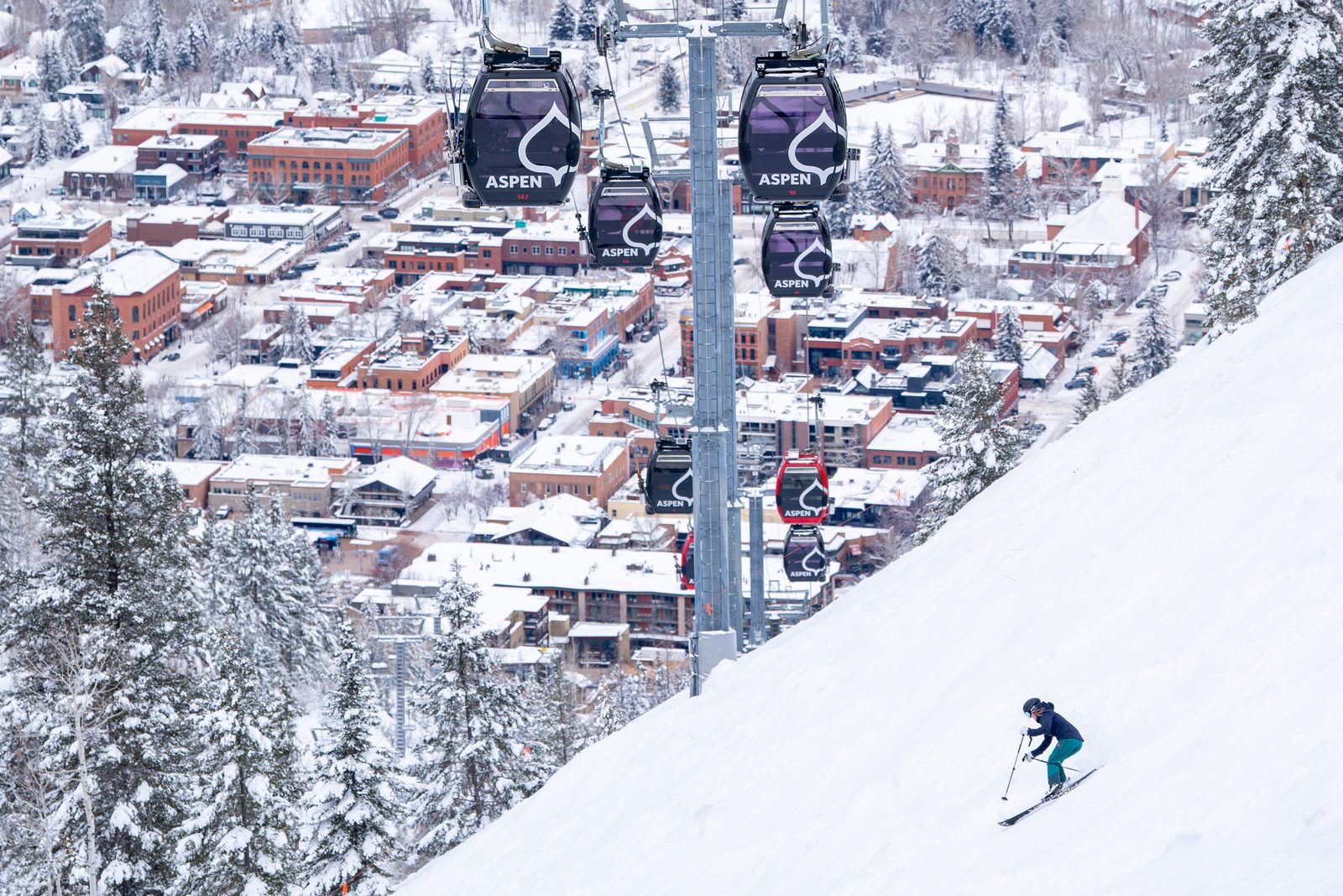 Esquiadora bajando por Aspen Mountain con el pueblo y las cabinas al fondo